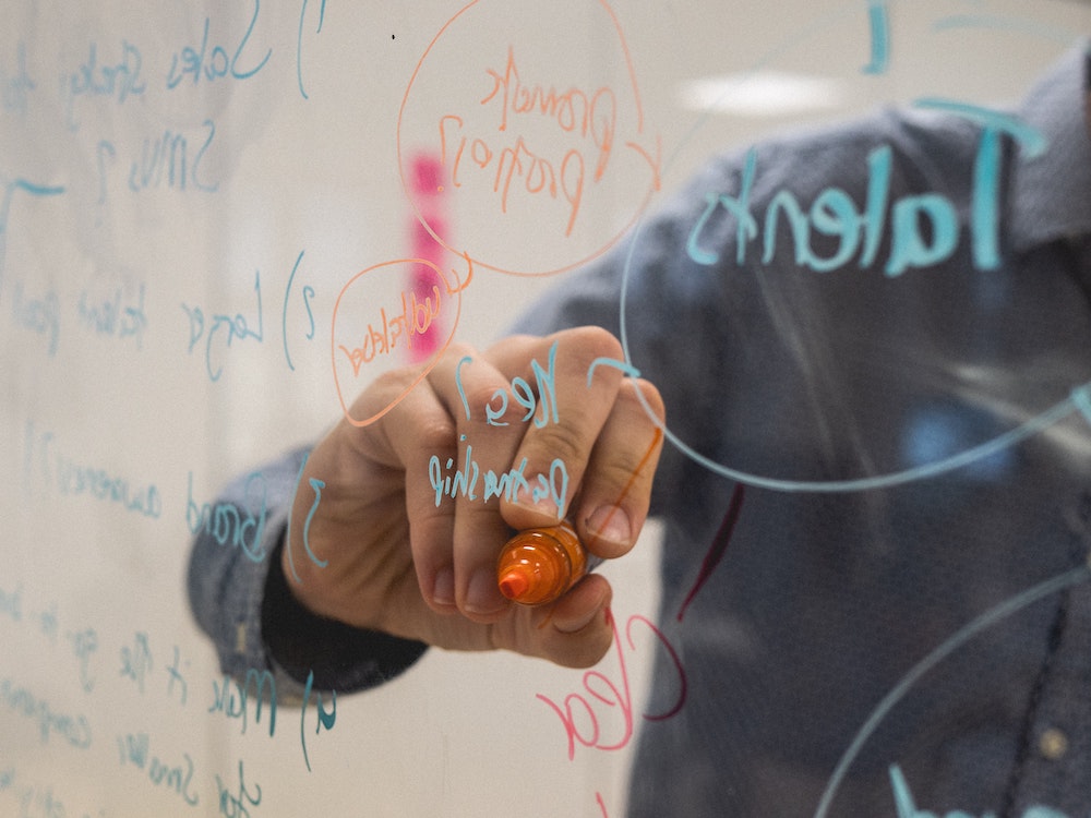 A mans hand writing on a glass window in orange pen.