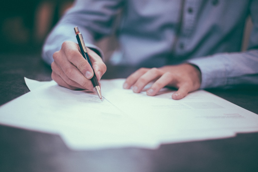 Mans hands as he writes on loose sheets of paper with a pen.