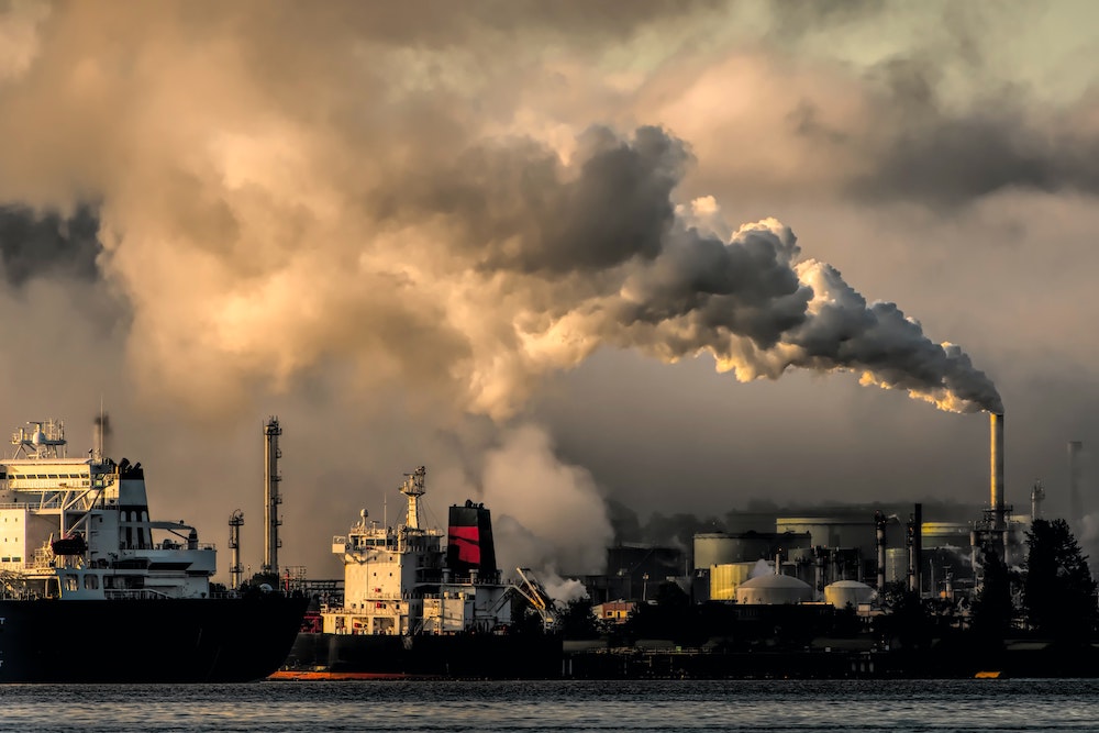 Water side factories spew smoke into the air from large chimneys.