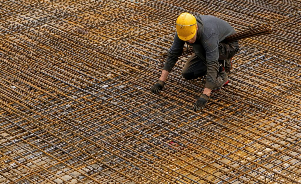 Construction worker wearing hard hat crouches on a grid of rebar