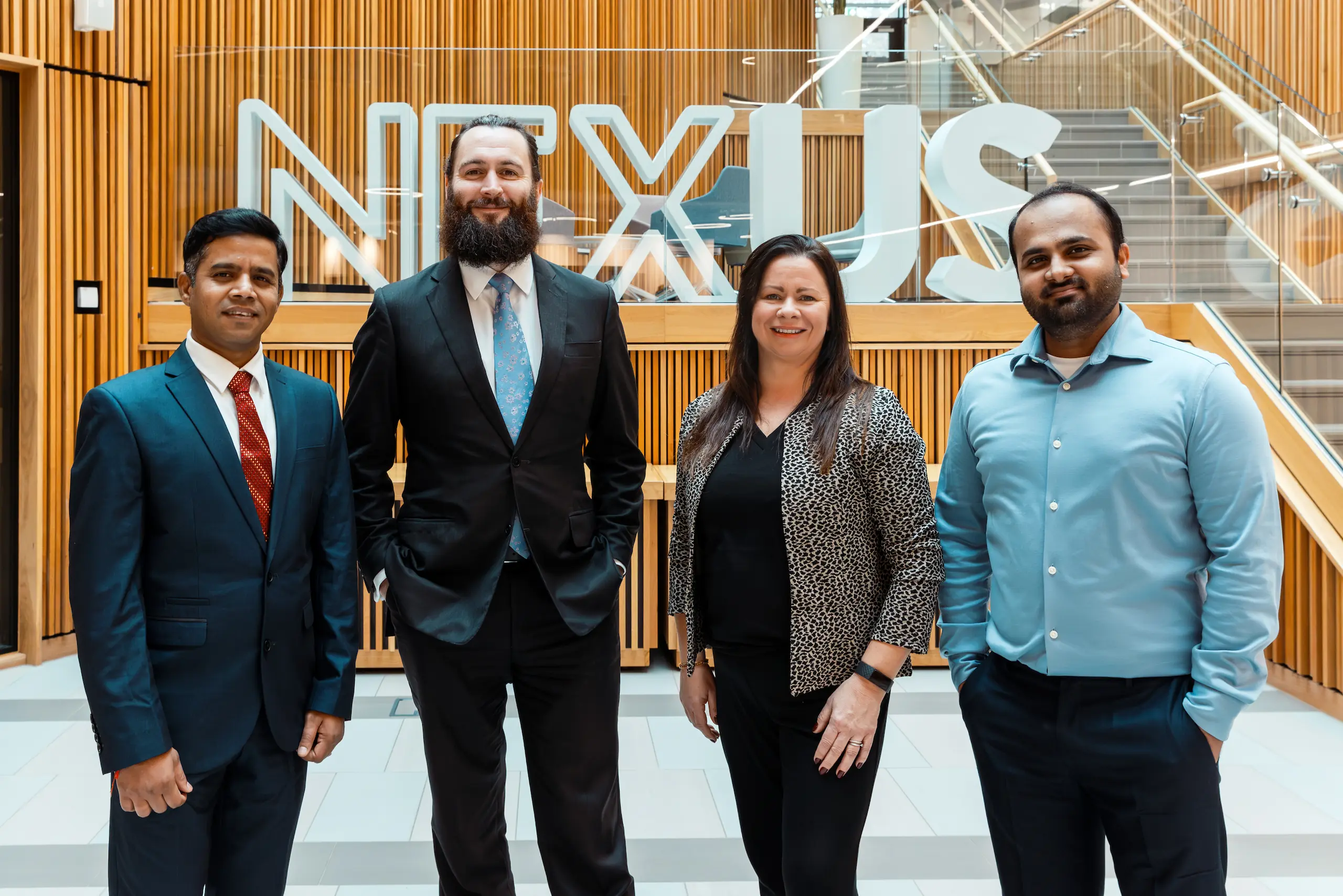Four people standing in front of NEXUS sign and staircase.